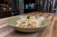 Bowl of Czech Potato Salad with peas, diced carrot, and corn, topped with a parsley sprig.