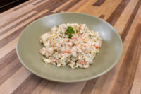 Bowl of Czech Potato Salad with creamy dressing, diced carrot, and peas on a wood table
