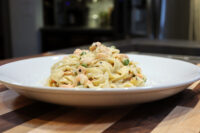 Plated Fettuccine Alfredo with Salmon, creamy pasta with pink salmon pieces and peas on a white dish.