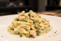 Plated Fettuccine Alfredo with Salmon, peas and cracked pepper in creamy sauce on white dish.