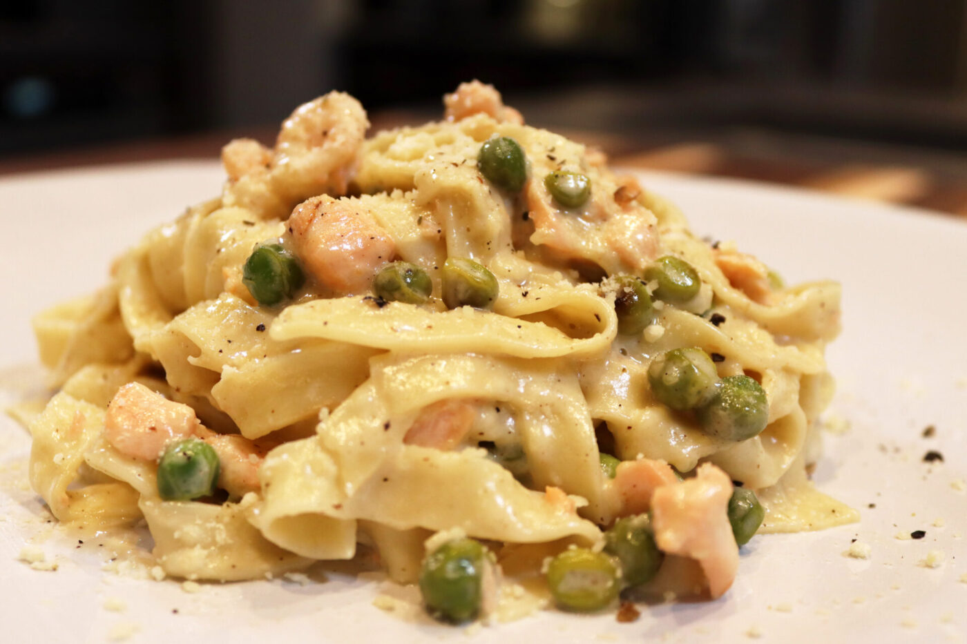 Plate of Fettuccine Alfredo with Salmon, showing creamy pasta, peas, and flaked salmon under grated cheese and pepper.