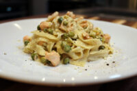 Plated Fettuccine Alfredo with Salmon topped with peas, grated cheese, and cracked black pepper.