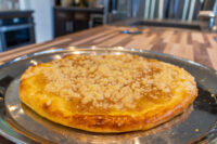 Whole Frgal Kolach with golden streusel crust on a metal plate over a wooden counter.