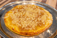 Round Frgal Kolach with golden streusel crust on a metal tray over a wood table.