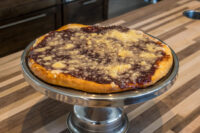 Round Frgal Kolach with Plum Filling and streusel topping, shown whole on a metal cake stand.