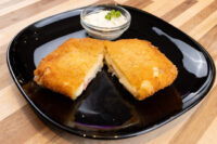 Fried Cheese with Ham cut in half showing melted cheese and ham, served with a creamy dip on a black plate