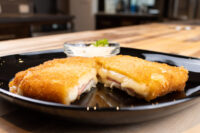 Fried Cheese with Ham cut in half showing melted cheese and ham, on a black plate with a creamy dip.