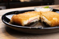 Fried Cheese with Ham sliced open on a black plate, showing melted cheese and ham, with a dip alongside.