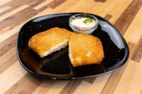 Halved Fried Cheese with Ham on a black plate, showing melted cheese and ham, with a dip alongside