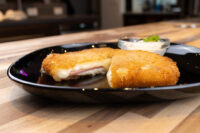 Fried Cheese with Ham cut in half showing melted cheese and ham, served on a black plate with dip.