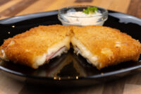 Halved Fried Cheese with Ham showing melted cheese and ham inside crispy breading, with dip on black plate