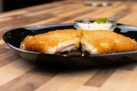 Halved Fried Cheese with Ham showing melted cheese and ham inside crispy breading, on a black plate.