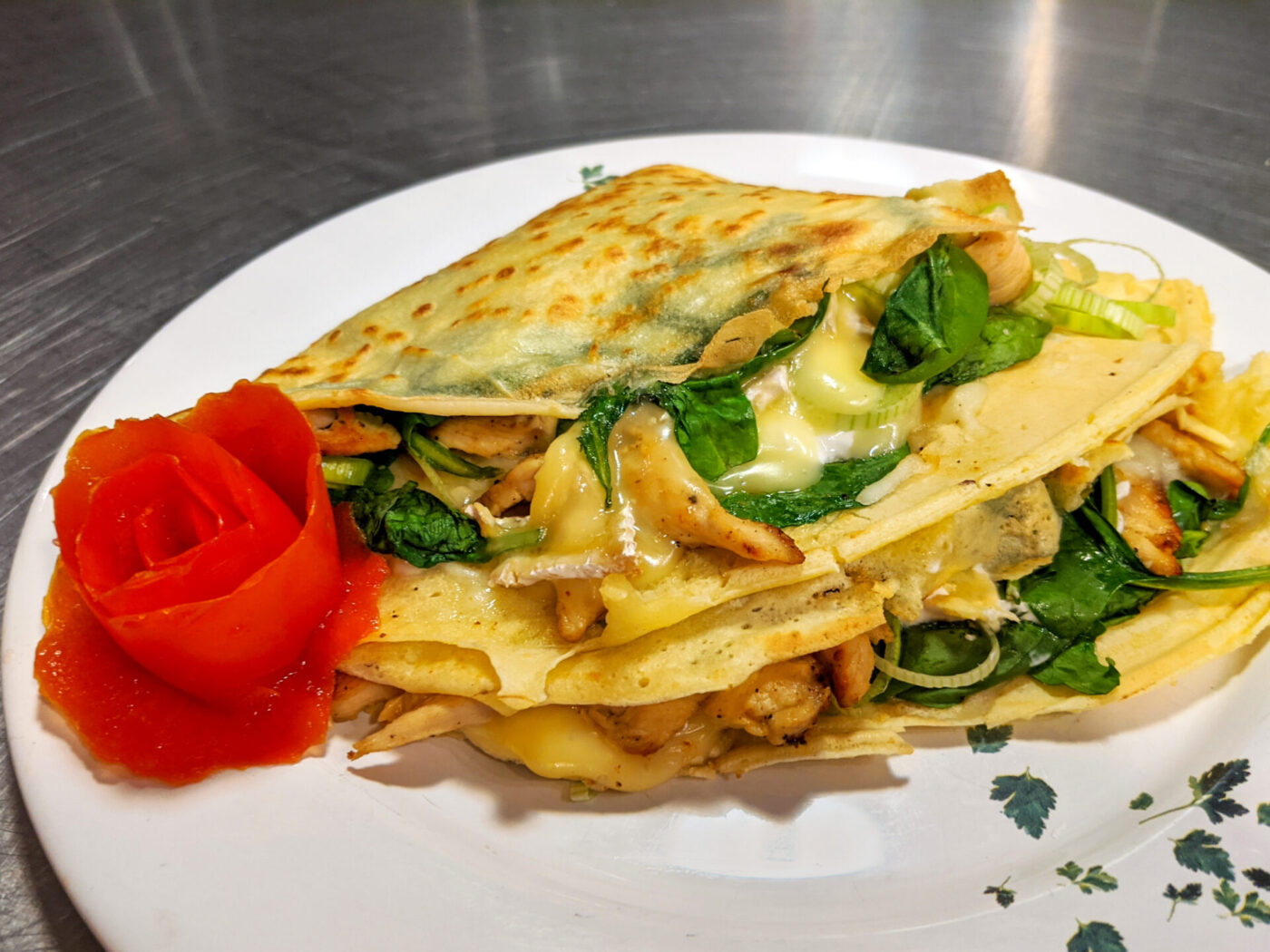 Galettes with Chicken, Spinach, and Brie Cheese folded into a wedge on a white plate with a tomato rose garnish.