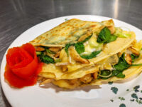 Galettes with Chicken, Spinach, and Brie Cheese folded into a wedge on a white plate with a tomato rose garnish.