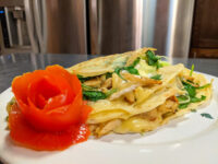 Galettes with Chicken, Spinach, and Brie Cheese, folded and sliced open on a plate with a tomato rose garnish