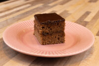A square Gingerbread Bar with dark chocolate coating on a pink scalloped plate.