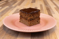 Square Gingerbread Bars slice with dark preserve filling and chocolate glaze on a pink plate.