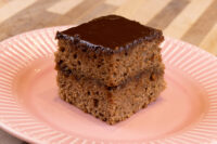 Square Gingerbread Bar with chocolate glaze and dark filling between two layers, on a pink plate