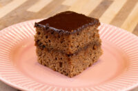 Square Gingerbread Bar with dark chocolate coating and two visible layers, on a pink ridged plate.