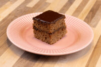 Square Gingerbread Bar with dark chocolate coating and two cake layers, on a pink ridged plate.