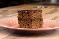 Two stacked squares of Gingerbread Bars topped with glossy chocolate coating, on a pink ridged plate.