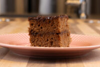 Square Gingerbread Bars with two dark layers and a glossy chocolate top, on a pink ridged plate.