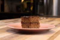 A square of Gingerbread Bars with a dark glossy coating, stacked in two layers on a pink plate.