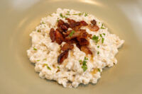 Plate of Halušky with Bryndza Cheese Substitution topped with crispy bacon and herbs on an olive-green plate