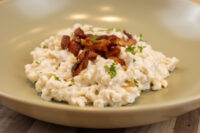 Halušky with Bryndza Cheese Substitution, creamy potato pasta topped with crispy bacon and herbs on a beige plate