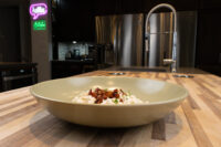 Bowl of Halušky with Bryndza Cheese Substitution topped with crispy bits and herbs on a butcher-block island.