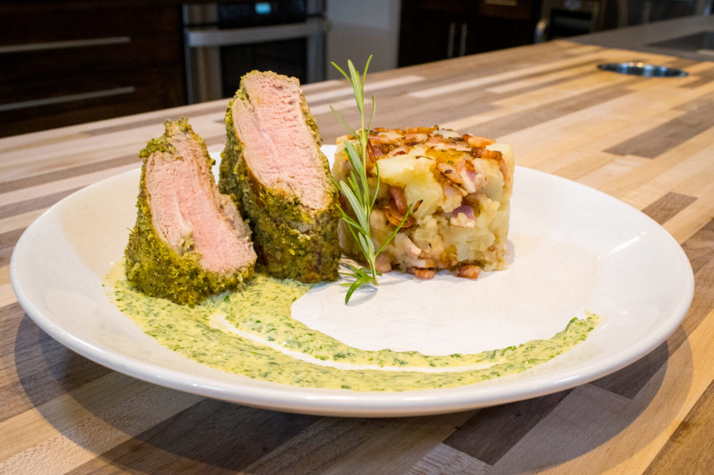 Sliced Herb-crusted Pork Tenderloin with pink center, herb sauce swirl, rosemary sprig, and potato-bacon hash
