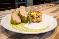 Sliced Herb-crusted Pork Tenderloin with pink center, herb sauce swirl, rosemary sprig, and potato-bacon hash