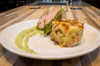 Sliced Herb-crusted Pork Tenderloin with rosemary, served with a potato cake and green herb sauce.