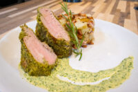Sliced Herb-crusted Pork Tenderloin with pink center beside roasted potatoes and green herb sauce