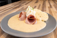 Horseradish Sauce Křenová Omáčka pooled on a plate with rolled ham slices and a bread roll
