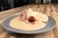Horseradish Sauce Křenová Omáčka pooled on a plate with rolled ham, whipped topping, and a biscuit.