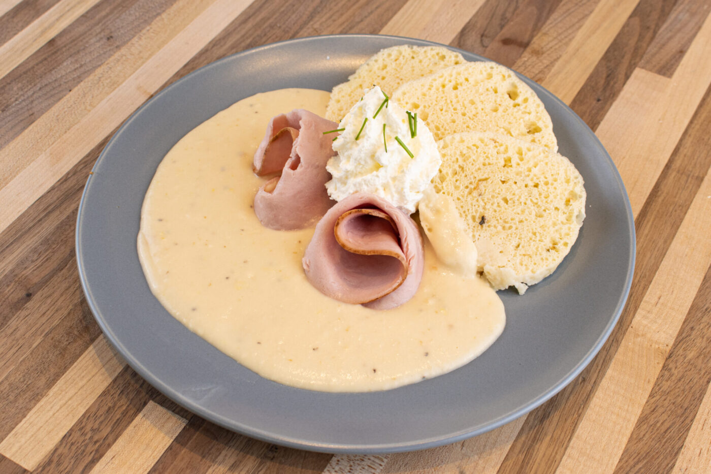 Horseradish Sauce Křenová Omáčka pooled on a plate with folded ham, whipped cream, and biscuits