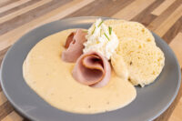 Horseradish Sauce Křenová Omáčka pooled on a plate with rolled ham and bread slices