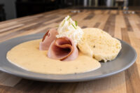 Horseradish Sauce Křenová Omáčka pooled on a plate with rolled ham slices and a biscuit.