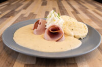 Horseradish Sauce Křenová Omáčka pooled on a grey plate with rolled ham and a cream dollop.