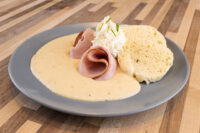 Horseradish Sauce Křenová Omáčka pooled on a plate with rolled ham, whipped cream, and a muffin