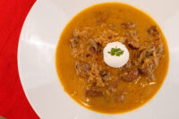 Bowl of Kapustnica Soup with sauerkraut, meat chunks, mushrooms, sour cream and parsley on a white plate