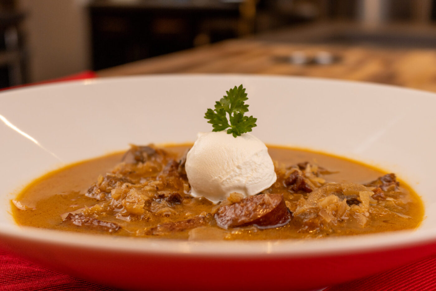 Bowl of Kapustnica Soup with sausage and sauerkraut, topped with cream and a parsley sprig.