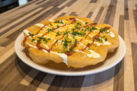 Langos flatbread topped with melted cheese, sour cream, red sauce, and chives on a white plate.