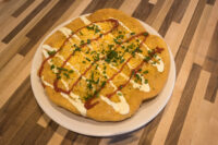 Fried Langos flatbread on a plate with red sauce, sour cream drizzle, shredded cheese, and chives