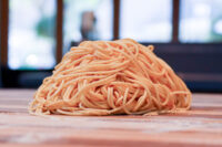 A mound of pale lo mein noodles for Lo Mein with Chicken resting on a wooden surface.