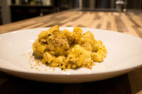 Plated Mac & Cheese topped with golden toasted breadcrumbs on a white dish over a wooden table