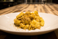 Plate of Mac & Cheese topped with golden herb breadcrumbs, set on a wooden table.