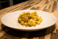 White plate of baked Mac & Cheese with a golden herb crumb topping on a wooden table.