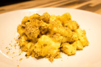 Close-up of Mac & Cheese with creamy sauce and golden herb breadcrumb topping on a white plate.